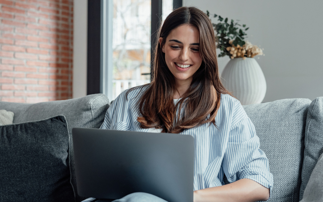 Smiling woman using a laptop sitting on couch Smiling Woman Using A Laptop Sitting On Couch